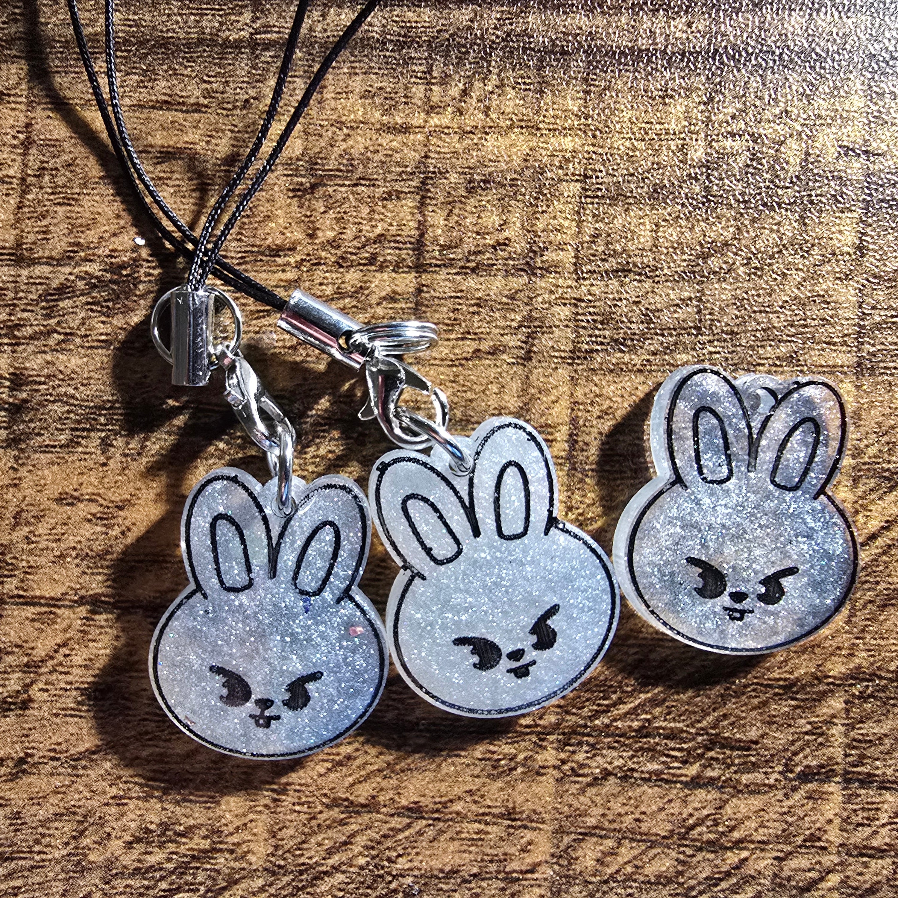 Three shimmery white Leebit bunny-shaped charms on a wooden surface
