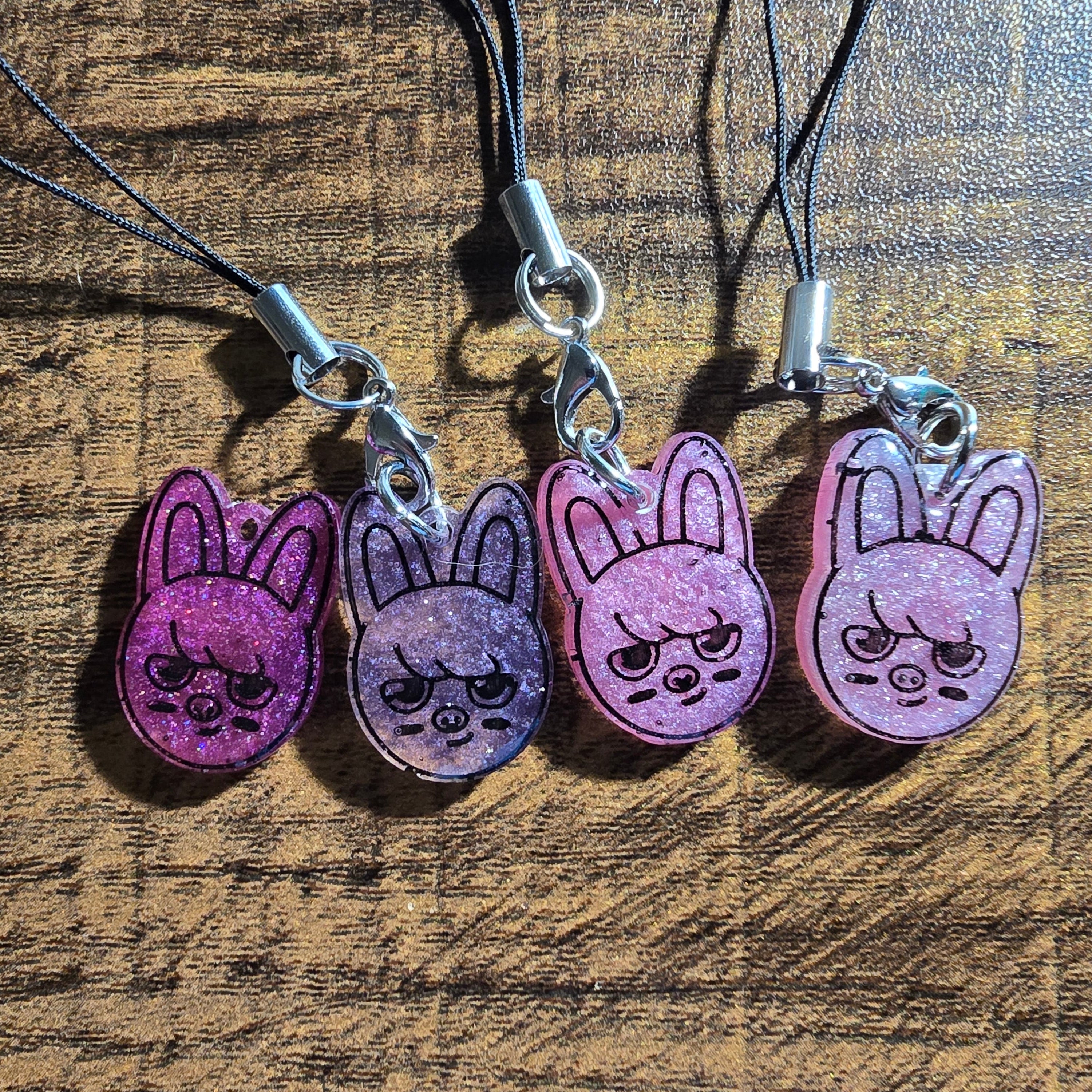 Four pink dwaekki bunny-shaped charms on black strings against a wooden background